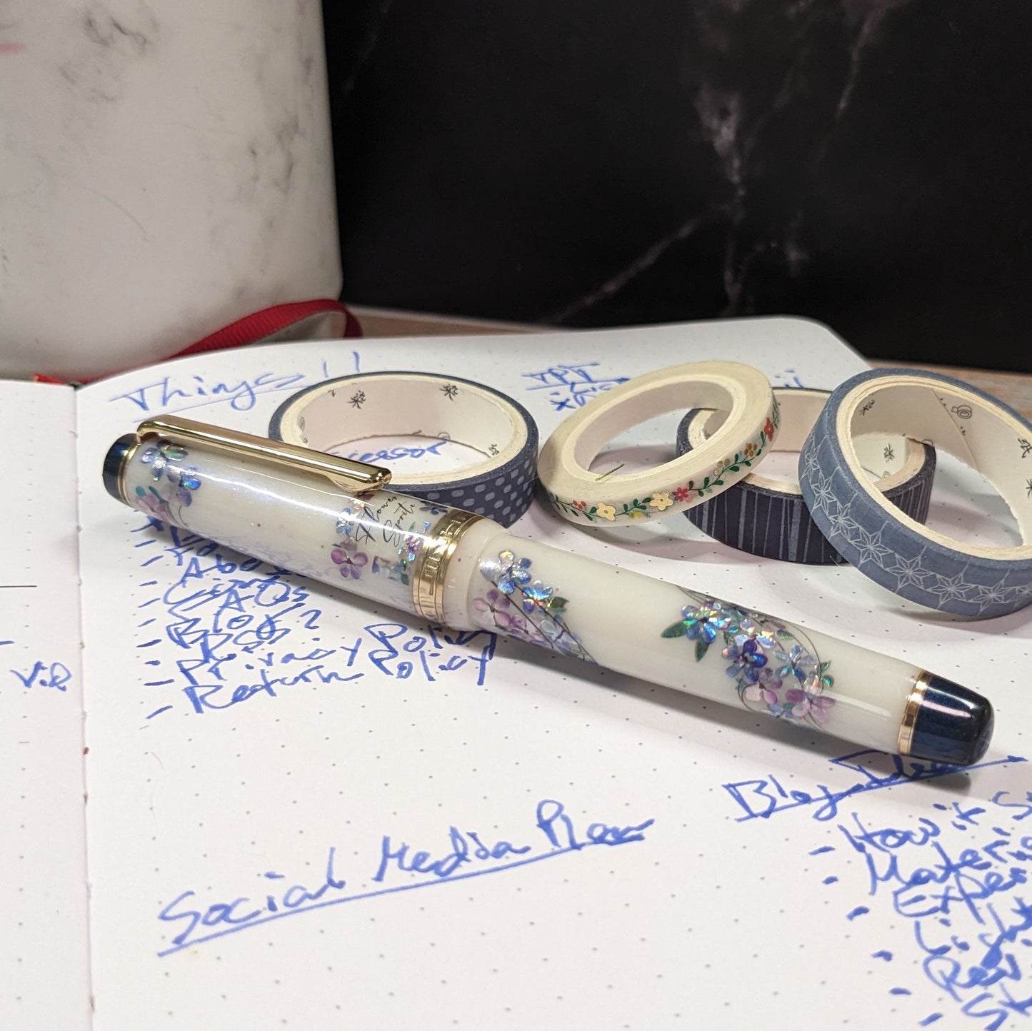 Fountain pen with floral design on a notebook page with writing and washi tape.