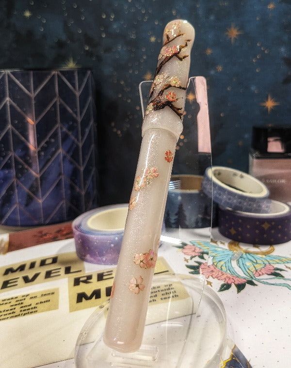 Decorative pen with floral designs on a clear stand against a blurred background