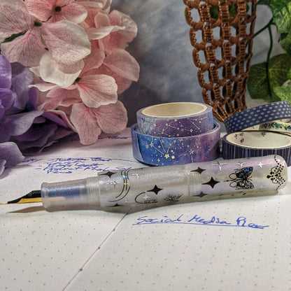 Decorative pen with star designs on a piece of paper with writing, surrounded by colorful washi tape and flowers.