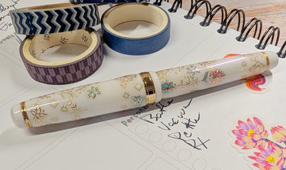 Decorative pen with floral designs on a white surface with tape and stationery items.