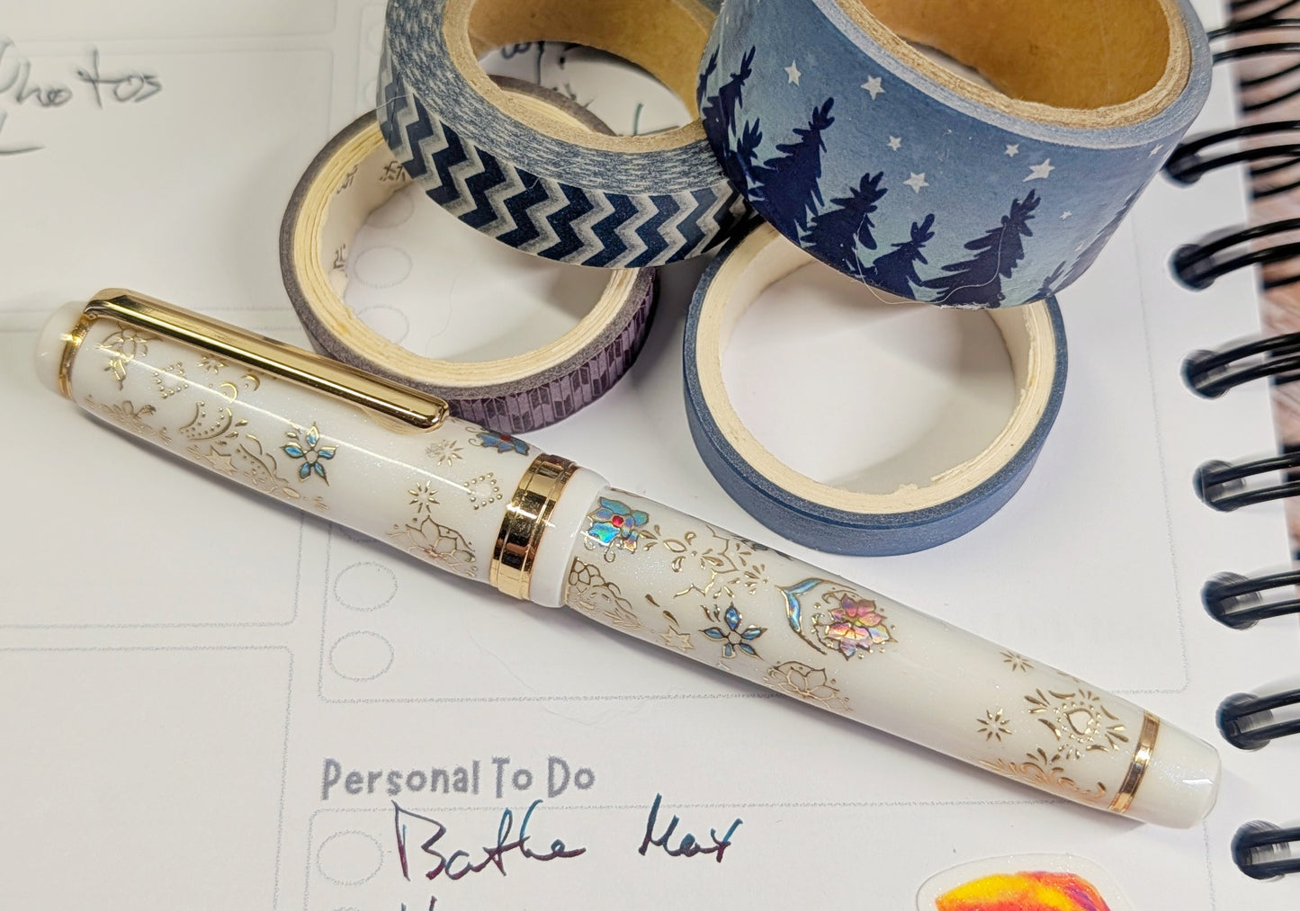 Decorative pen with floral patterns on a notebook page with washi tape in the background