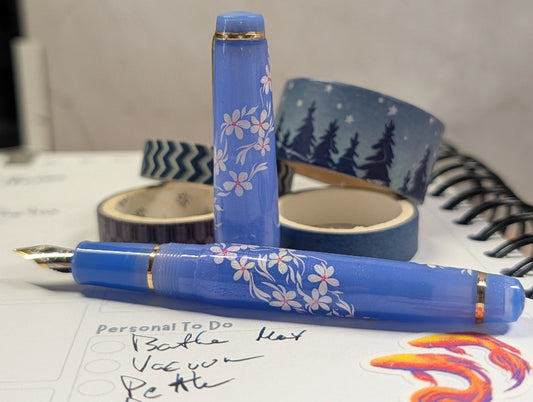 Purple pen with floral designs on a notebook with writing and colorful washi tape.