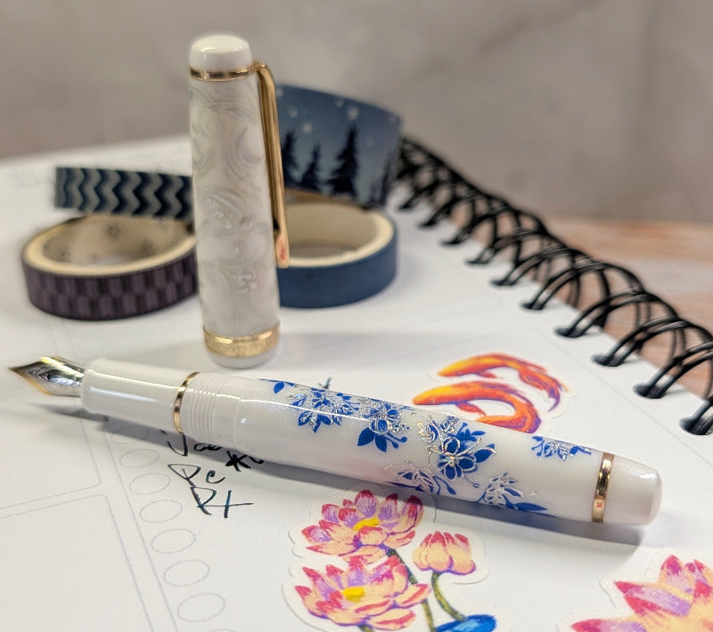 Decorative white fountain pen with blue floral design on a wooden surface