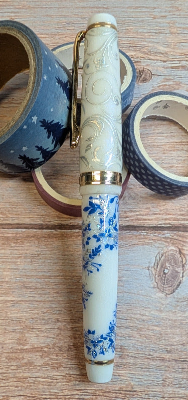 Decorative white fountain pen with blue floral design on a wooden surface